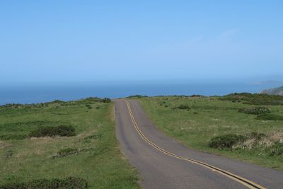 Road leading towards green landscape against sky