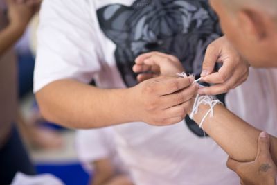 Midsection of man tying thread on friend hand