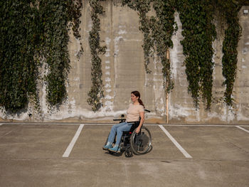 Disabled woman sitting on wheelchair against wall