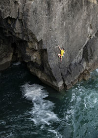 Young male rock climber climbing cliff above water