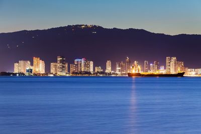 Illuminated cityscape by sea against sky at night