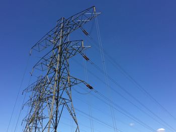 Low angle view of electricity pylon against clear blue sky