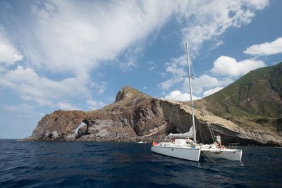 Sailboat sailing on sea by mountains against sky