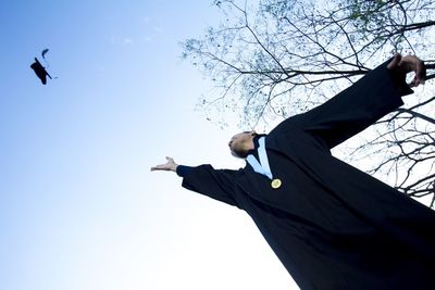 Low angle view of man flying mortarboard against clear sky