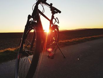 Bicycle by road against sky during sunset