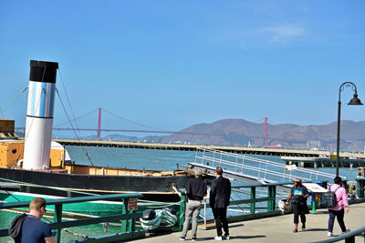 People walking on bridge over sea against clear blue sky