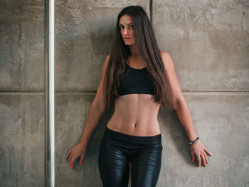 Portrait of sensuous pole dancer with long hair standing against wall in studio