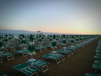 Chairs on beach against clear sky during sunset