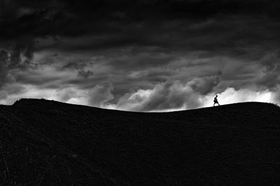 Low angle view of man walking on hill against cloudy sky