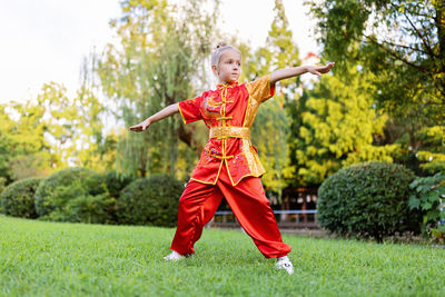 Full length of boy playing with arms raised standing on grassy field