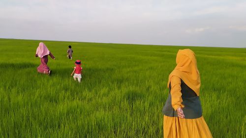 Rear view of people standing on field against sky