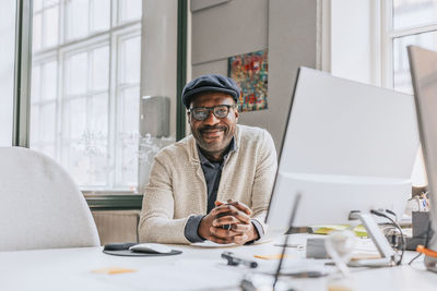 Portrait of smiling businessman with hands intertwined at desk in office