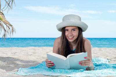 Portrait of young woman on book at beach against sky