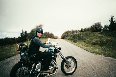 Portrait of man riding motorcycle on road against sky