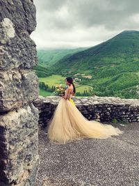 Woman holding bouquet while standing on mountain against sky