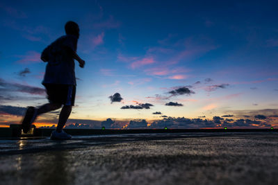 Rear view of silhouette man running on walkway at sunset