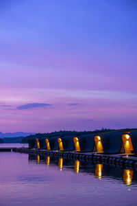 Illuminated bridge over sea against sky at sunset