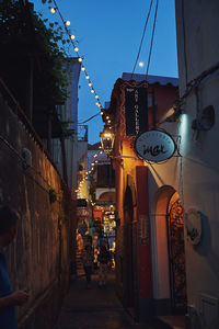 People on illuminated alley amidst buildings in city