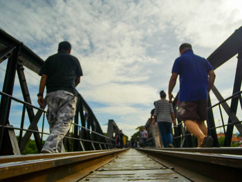 Rear view of men standing on footbridge against sky