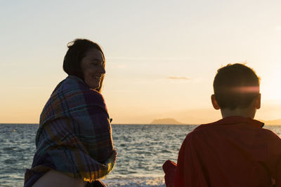 Mother and son at beach against sea and sky during sunset