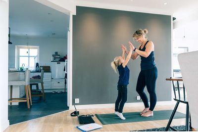 Smiling mother and daughter giving high-five while standing on mat in living room