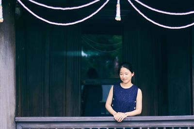 Portrait of smiling young woman standing against curtain