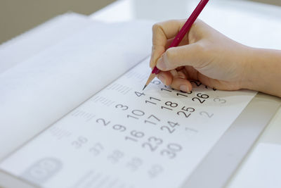 Cropped hand of person writing in calendar with pencil