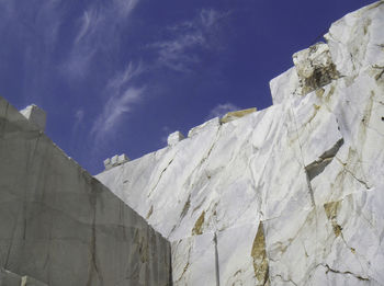 Low angle view of snow covered rocks against blue sky