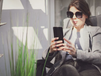 Young beautiful caucasian girl holds a smartphone in front of her while sitting in a garden chair