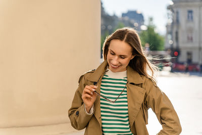 A woman smiles and holds sunglasses while walking in the city