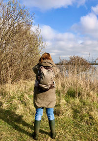 Rear view of woman standing on field looking over a lake