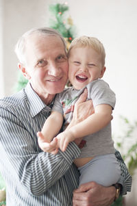 Handsome gray-haired caucasian grandfather hugs a little boy grandson against the christma tree