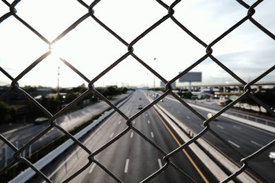 Road seen through chainlink fence against sky