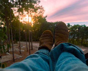 Low section of man in shoes relaxing outdoors against sky during sunset