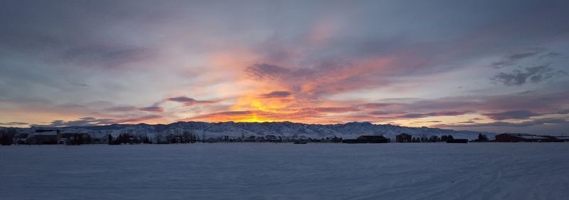 Panoramic shot of snow covered field against cloudy sky during sunset