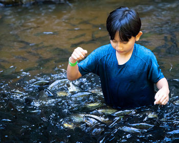 High angle view of boy standing in water with school of fish