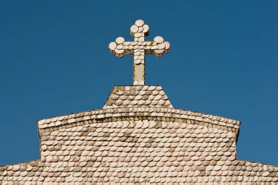 Low angle view of cross on roof of building against clear blue sky