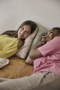 Multiracial female friends lying in bed while resting at home