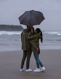 Rear view of woman with umbrella standing at beach