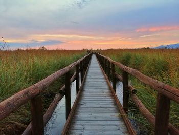 Wooden footbridge on field against sky during sunset