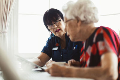 Caretaker assisting senior woman in using digital tablet at home