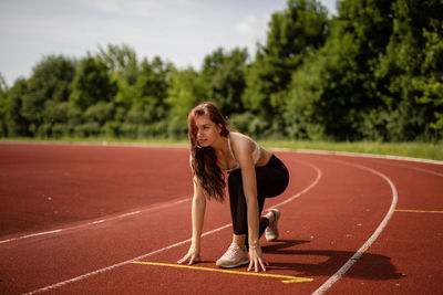 Full length of young woman at starting line on sports track