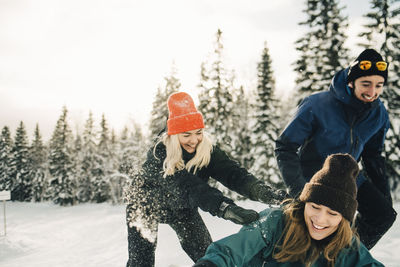 Happy male and female friends playing at ski resort during winter