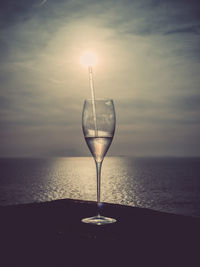 Close-up of wineglass against sea during sunset