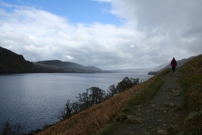 Rear view of woman walking at lake against sky