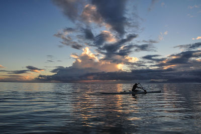 Silhouette people on sea against sky during sunset