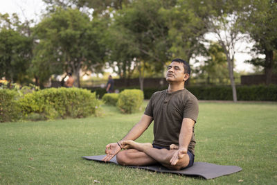 Full length of man sitting on grass against trees