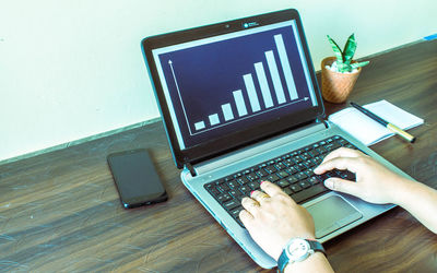 Midsection of man using laptop with smart phone and plant on table