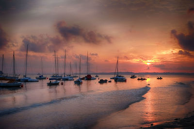 Sailboats moored on sea against sky during sunset