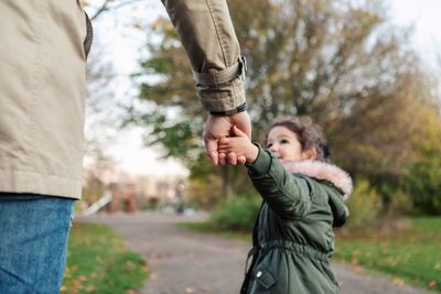 Daughter pulling father while holding hands in park during autumn